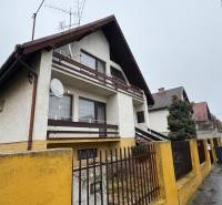 NA PREDAJ veľký rodinný dom v obci Pusté Úľany Sládkovičovo - Rodinný dom s balkónom, anténou a žltým plotom v pokojnej ulici.