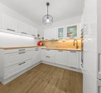 NOVOSTAVBA 2-IZB.BYT,ZÁHRADKA 26 m²,PARK.STÁTIE, MAHULANKA,PEZINOK - Kuchyňa s bielymi skrinkami, drevenými doskami a podlahou s dreveným dekorom v 2-izbovom byte.