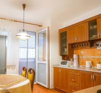 Predaj, 3 - izbový byt, Žiar nad Hronom - Kuchyňa v 2-izbovom byte s drevenými skrinkami, jedálenským stolom a vstupom na balkón.