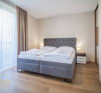 Lukratívne dvoj a štvorizbové byty v Tatranskej Lomnici na prenájom - Spálňa v 2-izbovom byte s pohodlnou posteľou, podlahou s dreveným dekorom a závesmi.