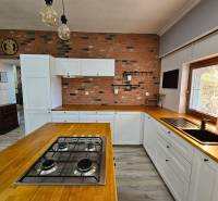 HD reality, predaj rodinný dom Štiavnické Bane - Kuchyňa v rodinnom dome s tehlovou stenou, drevenými doplnkami a podlahou s dreveným dekorom.