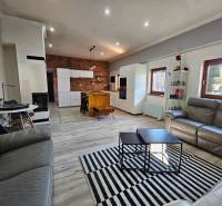 HD reality, predaj rodinný dom Štiavnické Bane - Obývacia izba s kuchyňou v rodinnom dome, podlaha s dreveným dekorom, tehlová stena.