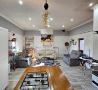 HD reality, predaj rodinný dom Štiavnické Bane - Obývačka v rodinnom dome s pohovkami, kuchyňou a podlahou s dreveným dekorom.