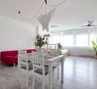 VELKOMETRÁŽNY 1 IZB.AP.BYT- TRNAVSKÁ CESTA, RUŽINOV, BRATISLAVA - Obývacia izba s bielym stolom, červeným gaučom a podlahou s dreveným dekorom.