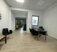 Na prenájom komerčné priestory v priemyselnej zóne v Trenčíne - Obchodné priestory s podlahou s dreveným dekorom, minimalistický nábytok a výrazné stoličky.