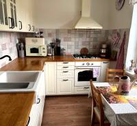 2-izbový byt v Seredi- bez rezervačnej zálohy - Kuchyňa 2-izbového bytu s podlahou s dreveným dekorom, biele skrinky, kvety a dekorácie.