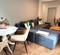 2-izbový byt v Seredi- bez rezervačnej zálohy - Obývacia izba s podlahou s dreveným dekorom, pohodlnou sedačkou a jedálenským stolom.