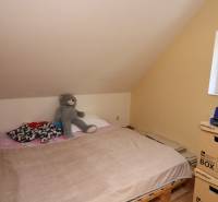 ZNÍŽENÁ cena - viacgeneračný  rodinný dom v Borinke  - Spálňa s paletovou posteľou, hnedou prikrývkou a mackom pri okne v podkroví.