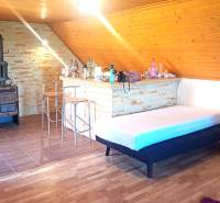 Predaj chaty a chalupy, Levice - Interiér chaty s krbom, barovým pultom a podlahou s dreveným dekorom.