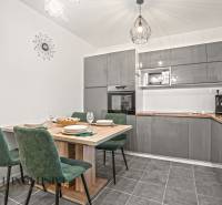 NA PREDAJ MODERNÝ 3-IZB. RD TYPU BUNGALOV V GABČÍKOVE - Kuchyňa v rodinnom dome so sivou linkou, jedálenským stolom a zelenými stoličkami.