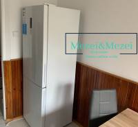 Na predaj prakticky riešený 2-izbový byt s balkónom - Kuchyňa v 2-izbovom byte, chladnička, drevený obklad, šedá stolička, jedálenský stôl.