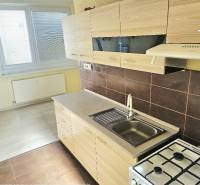 2,5 izbový byt Bánovce nad Bebravou/CENTRUM- STRED/KOMLETNÁ REKONŠTRUK - Kuchyňa v 2-izbovom byte s bielymi skrinkami a podlahou s dreveným dekorom.