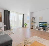 BÝVANIE VO VILA DOME - POSLEDNÝ VOĽNÝ 3-IZBOVÝ BYT SO ZÁHRADOU - Svetlá obývačka v 3-izbovom byte, podlaha s dreveným dekorom, biely nábytok.