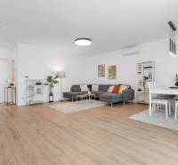 BÝVANIE VO VILA DOME - POSLEDNÝ VOĽNÝ 3-IZBOVÝ BYT SO ZÁHRADOU - Priestranná obývacia izba s podlahou s dreveným dekorom a sedačkou v 3-izbovom byte.