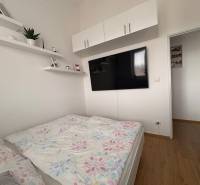 Prenájom moderného 2-izbového bytu v centre Komárna, 40 m² – Petőfiho  - Svetlá spálňa v 2-izbovom byte s TV a podlahou s dreveným dekorom.