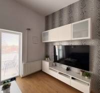 Prenájom moderného 2-izbového bytu v centre Komárna, 40 m² – Petőfiho  - Obývacia izba s TV stenou, vzorovanou tapetou a podlahou s dreveným dekorom v 2-izbovom byte.