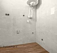 ALL INCLUSIVE I 3 IZBOVÉ BYTY S TERASOU, SO ZÁHRADOU + 2 PARK. MIESTA - Kúpeľňa s vodným ohrievačom a podlahou s dreveným dekorom v 3-izbovom byte.