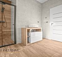 ALL INCLUSIVE I 3 IZBOVÉ BYTY S TERASOU, SO ZÁHRADOU + 2 PARK. MIESTA - Kúpeľňa v 3-izbovom byte s podlahou s dreveným dekorom, skleneným sprchovým kútom a modernou sanitou.