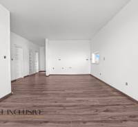 ALL INCLUSIVE I 3 IZBOVÉ BYTY S TERASOU, SO ZÁHRADOU + 2 PARK. MIESTA - Priestranná miestnosť v 3-izbovom byte s bielymi stenami a podlahou s dreveným dekorom.