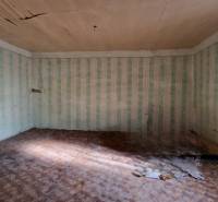 Vidiecky dom v Zemplínskej Teplici - Izba v rodinnom dome s poškodeným stropom, tapetami a podlahou s dreveným dekorom.