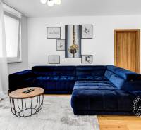 Krásny 3i byt, LODŽIA, PARKING, Dúbravka, Cabanova - Obývacia izba s tmavomodrou sedačkou, podlahou s dreveným dekorom a dekoráciami na stene.