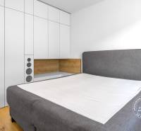 Krásny 3i byt, LODŽIA, PARKING, Dúbravka, Cabanova - Svetlá spálňa s veľkým šatníkom, sivou posteľou a podlahou s dreveným dekorom v 3-izbovom byte.