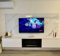 PRENÁJOM - 3-izbový veľkometrážny byt v RED OAK, Lužianky -REZERVOVANÉ - Obývacia izba v 3-izbovom byte s televízorom, policami a podlahou s dreveným dekorom.