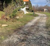 Pozemok 5.200 m2 , šírka 35 m, Horné Jabloňovce (SM - 849)   - Rekreačné pozemky Horné Jabloňovce v Jabloňovciach s chodníkom vedľa malého domu a stromami.