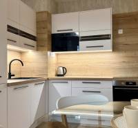 Na prenájom novostavba 2i bytu s parkingom, PRÚDY I., Trnava - Kuchyňa v 2-izbovom byte s bielymi skrinkami, čiernym drezom a podlahou s dreveným dekorom.