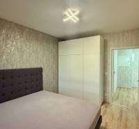 Na prenájom novostavba 2i bytu s parkingom, PRÚDY I., Trnava - Spálňa s posteľou, bielou skriňou a podlahou s dreveným dekorom v 2-izbovom byte.