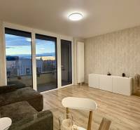 Na prenájom novostavba 2i bytu s parkingom, PRÚDY I., Trnava - Obývacia izba so sedacou súpravou a podlahou s dreveným dekorom, 2-izbový byt.