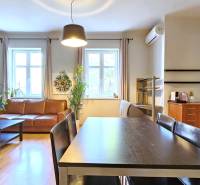 PRIESTRANNÝ 2.IZB. BYT - PIVNICA, LODŽIA - DOBROVSKÉHO, STARÉ MESTO - Obývacia izba s podlahou s dreveným dekorom, koženou sedačkou a kameňom na stene v 2-izbovom byte.