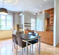 PRIESTRANNÝ 2.IZB. BYT - PIVNICA, LODŽIA - DOBROVSKÉHO, STARÉ MESTO - Obývačka s podlahou s dreveným dekorom, pohovkou, jedálenským stolom a kuchynským kútom v 2-izbovom byte.