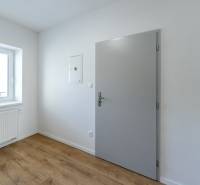 Moderný, priestranný 2i byt 70m2, v tichom dvore, úplne nový - Interiér izby s bielymi stenami, podlahou s dreveným dekorom a oknom.