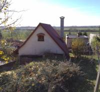 Štýlový rekreačný domček Levice - Chata v Starých Leviciach, rekreačná lokalita, obklopená prírodou a kríkmi, v pozadí pole.