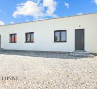 IDEÁLNY 1 IZBOVÝ BYT | VEĽKÉ RIPŇANY | TOPOĽČANY - Jednopodlažná budova s bielou omietkou a štrkovým parkoviskom na Hlohovskej ceste vo Veľkých Ripňanoch.