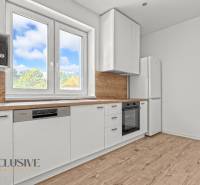 IDEÁLNY 1 IZBOVÝ BYT | VEĽKÉ RIPŇANY | TOPOĽČANY - Svetlá kuchyňa s bielymi skrinkami, podlaha s dreveným dekorom, okno s výhľadom.