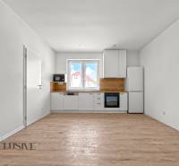 IDEÁLNY 1 IZBOVÝ BYT | VEĽKÉ RIPŇANY | TOPOĽČANY - Minimalistická kuchyňa s bielymi skrinkami a podlahou s dreveným dekorom v 1-izbovom byte.