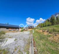 Stavebné pozemky v lokalite Slnečná úboč, Levočská Dolina - Pozemok na bývanie v Levočskej doline v Levoči s priľahlou vegetáciou a modrou oblohou.