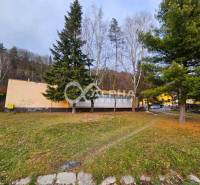 Budova s pozemkom, obec Helcmanovce, okres Gelnica - Budova v Helcmanovciach obklopená stromami, so susednou cestou a vozidlami.