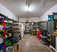 Budova s pozemkom, obec Helcmanovce, okres Gelnica - Miestnosť s regálmi, plechovými skrinkami a rôznymi predmetmi na podlahe s dreveným dekorom.