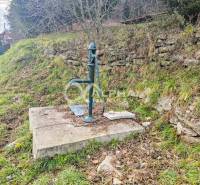 Budova s pozemkom, obec Helcmanovce, okres Gelnica - Ručná pumpa na betónovom základe vedľa kamennej steny v Helcmanovciach.