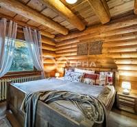 Zrubový rodinný dom, Veľká Lomnica - Spálňa v rodinnom dome s drevenými stenami, posteľou a kreslom, svetelnou atmosférou.