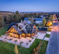 Zrubový rodinný dom, Veľká Lomnica - Rodinný dom na ulici Golfová, Veľká Lomnica, obklopený zeleňou a osvetlený večerom.