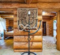 Zrubový rodinný dom, Veľká Lomnica - Interiér rodinného domu z guľatiny s vyrezávaným panelom a kovovým svietnikom.
