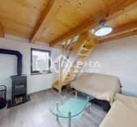 Exkluzívne záhradná chata, sídlisko Tarča, Spišská Nová Ves - Podkrovný interiér chaty s podlahou s dreveným dekorom, schodiskom, kachľovou pecou a skleneným stolíkom.