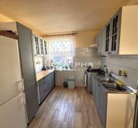 EXKLUZÍVNE Rodinný dom, širšie centrum, Spišská Nová Ves - Kuchyňa s šedými skrinkami, podlahou s dreveným dekorom a oknom s kvetmi v rodinnom dome.