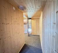 Vám ponúka na predaj rodinný dom v Komárne, ča - Drevené obloženie stien a stropu v chodbe rodinného domu s kobercom na podlahe.