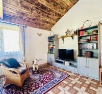 Vám ponúka na predaj rodinný dom v Komárne, ča - Interiér rodinného domu s dreveným dekorom, koberec, kreslo a úložná skrinka.