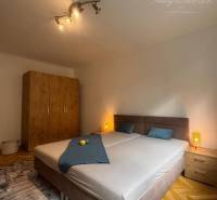 Vám ponúka 1 izbový byt vo VYHĽADÁVANEJ lokali - Spálňa v 1-izbovom byte so svetlom, skriňou a posteľou na podlahe s dreveným dekorom.